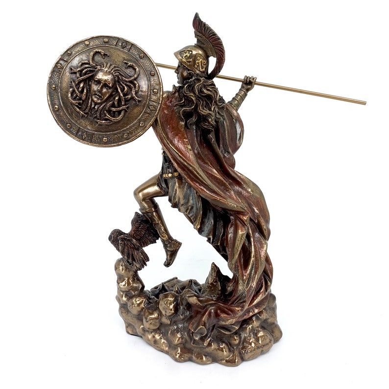 Puede incluir: Una estatua de bronce de una diosa griega, Atenea, sosteniendo una lanza y un escudo con una cabeza de Medusa. La estatua est&aacute; de pie sobre una base rocosa y tiene una capa roja que fluye.