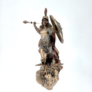 Puede incluir: Una estatua de bronce de Atenea, la diosa griega de la sabidur&iacute;a y la guerra, de pie sobre una base con un b&uacute;ho. Ella sostiene una lanza y un escudo, y su casco est&aacute; adornado con una cresta. La estatua est&aacute; pintada en tonos dorados, marrones y rojos.