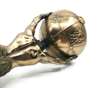 May include: Bronze sculpture of a muscular figure holding up a globe. The globe is decorated with symbols and designs.