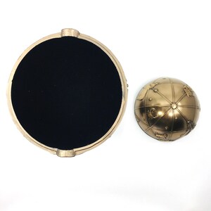 May include: A gold-coloured globe trinket box with a black velvet interior. The globe features a detailed map with constellations and zodiac signs.