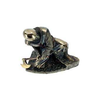 May include: A bronze figurine of a kneeling knight in chainmail armor holding an axe. The knight is wearing a red sash and has a helmet on his head. The figurine is set on a rocky base.