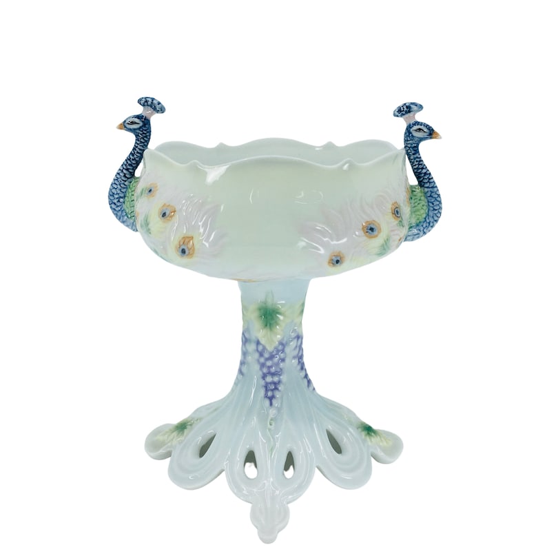 May include: A white ceramic peacock bowl with a scalloped rim. Two peacock figures are on the sides. The bowl has a pedestal base with a grape and leaf design. The base is shaped like a peacock's tail.