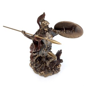 Puede incluir: Una estatua de bronce de Atenea, la diosa griega de la sabidur&iacute;a y la guerra, sosteniendo una lanza y un escudo. Est&aacute; de pie sobre una base rocosa con un b&uacute;ho a sus pies. La estatua est&aacute; inscrita con la palabra "ATHENA".