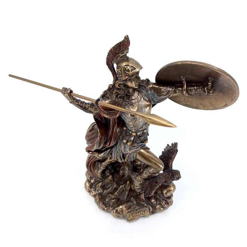Puede incluir: Una estatua de bronce de Atenea, la diosa griega de la sabidur&iacute;a y la guerra, sosteniendo una lanza y un escudo. Est&aacute; de pie sobre una base rocosa con un b&uacute;ho a sus pies. La estatua est&aacute; inscrita con la palabra "ATHENA".