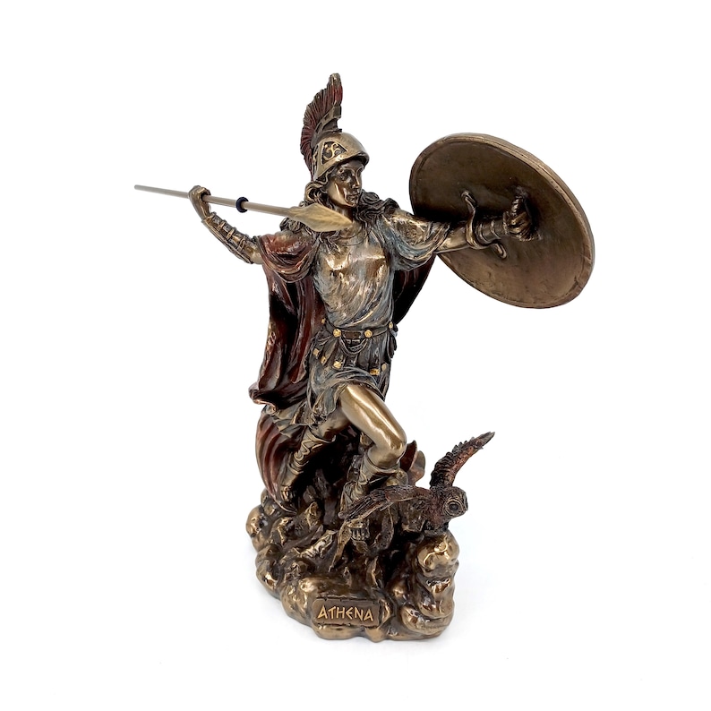 Puede incluir: Una estatua de bronce de Atenea, la diosa griega de la sabidur&iacute;a y la guerra, de pie sobre una nube con un b&uacute;ho a sus pies. Ella sostiene una lanza y un escudo, y su casco est&aacute; adornado con una pluma. La base de la estatua est&aacute; inscrita con la palabra "ATHENA".