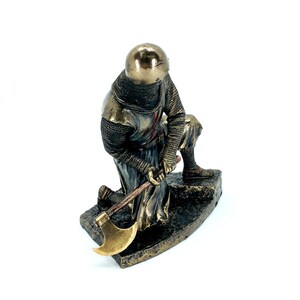 May include: A bronze statue of a kneeling crusader knight holding an axe. The knight is wearing chainmail armor and a helmet with a red cross on his chest.
