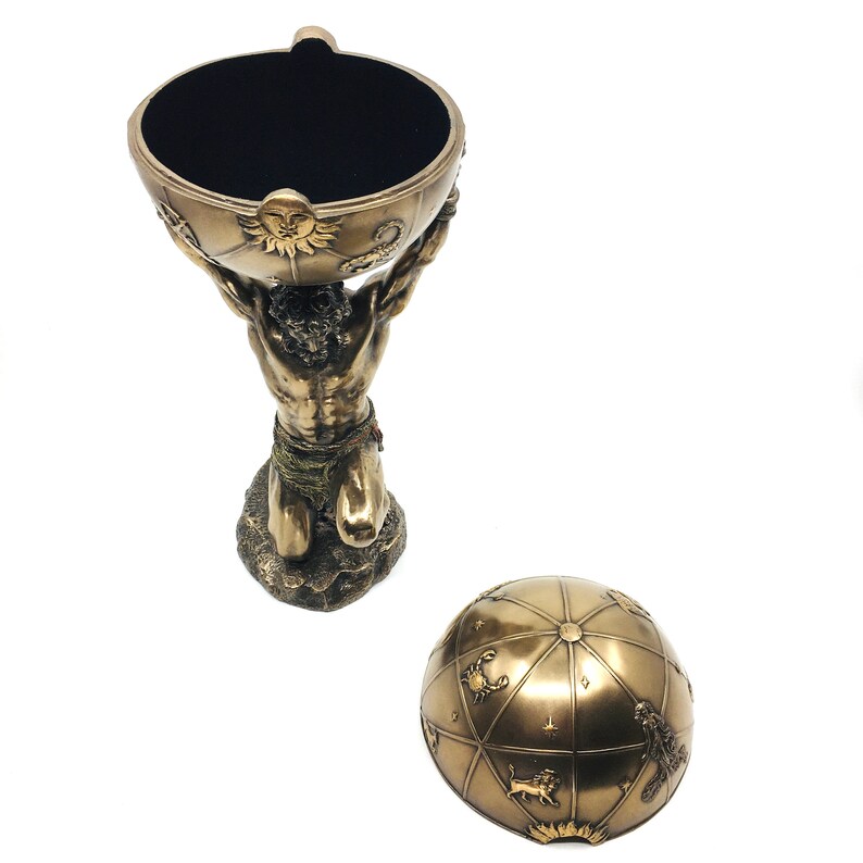May include: A bronze sculpture of a kneeling man holding a globe with zodiac signs on it. The globe is the lid of a decorative box.