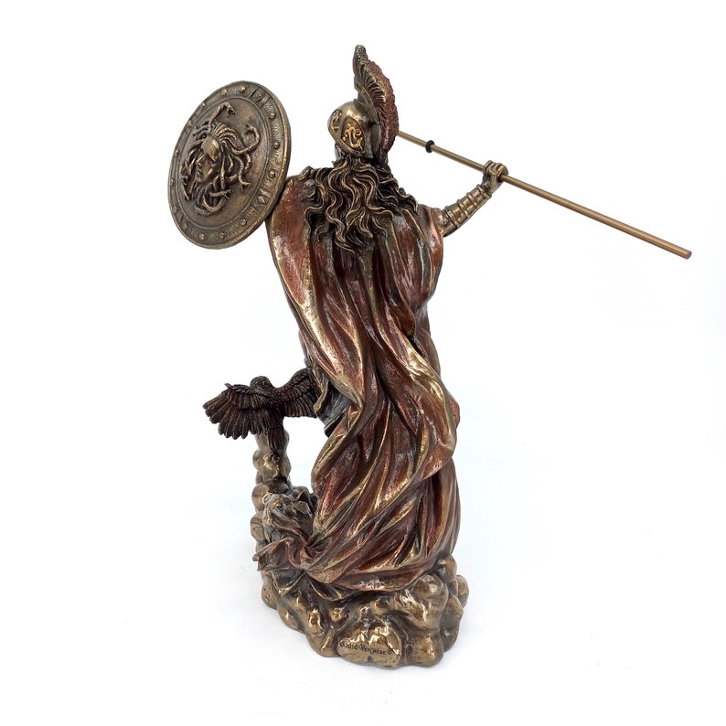 Puede incluir: Una estatua de bronce de una diosa griega, posiblemente Atenea, de pie sobre una base en forma de nube. Ella sostiene una lanza en su mano derecha y un escudo con una cabeza de Medusa en su mano izquierda. La estatua est&aacute; pintada en tonos dorados y marrones.