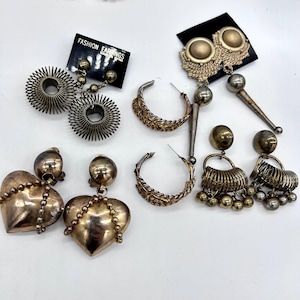 May include: A collection of five pairs of gold-tone metal earrings. The set includes circular coil earrings, textured hoop earrings, heart-shaped drop earrings with beaded accents, and two pairs of dangling earrings with spherical and conical components.
