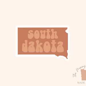 Pu&ograve; includere: Un adesivo con il contorno del Dakota del Sud in marrone con il testo "south dakota" in un font retr&ograve;. L'adesivo &egrave; su uno sfondo bianco.