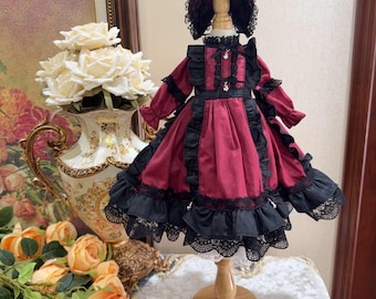 Puede incluir: Una muñeca con un vestido burdeos con ribete de encaje negro y un gorro de encaje negro. El vestido tiene un cuello con volantes y una cinta negra alrededor de la cintura.