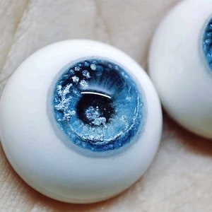 May include: Two realistic-looking blue glass eyes with white sclera and a blue iris with silver glitter.