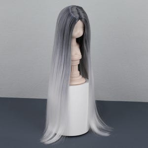 May include: A long, straight wig with a gray to white ombre effect. The wig is displayed on a mannequin head and is set against a neutral background. The hair is sleek and appears to be synthetic.
