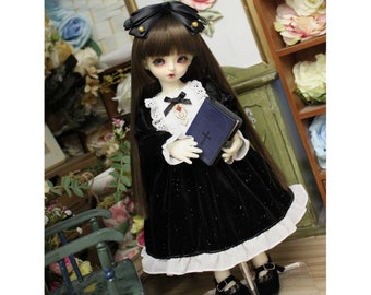 May include: A doll wearing a black velvet dress with a white lace trim and a black bow. The doll is holding a blue book with a cross on the cover. The doll has long brown hair and is wearing a black headband with a gold bow.