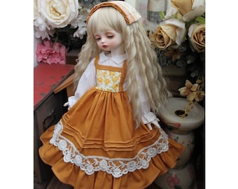 May include: A doll wearing a yellow and white floral print dress with a brown skirt and white lace trim. The doll has blonde hair and is wearing a white headband with a floral pattern.