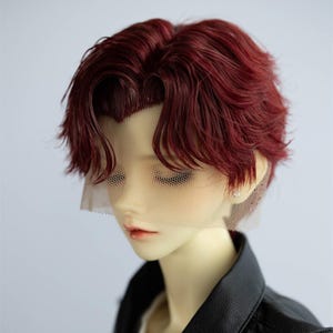 May include: A doll head with a short, wavy, burgundy wig. The wig has a natural-looking hairline and is styled with a side part. The doll is wearing a black jacket and has a mesh covering over its face.
