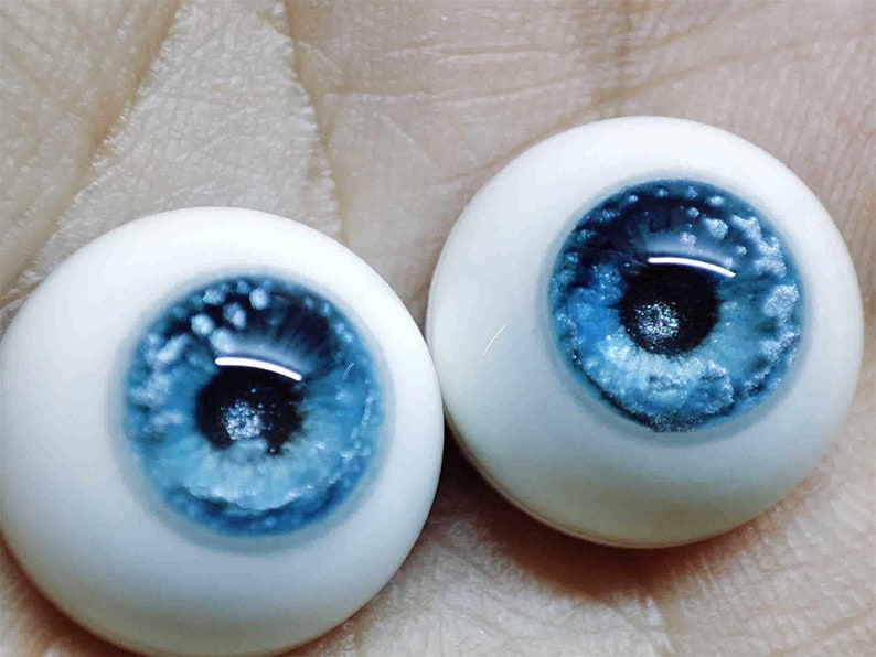 May include: Two blue and white doll eyes with a sparkly finish. The irises are a light blue with a darker blue ring around the pupil. The sclera is white.
