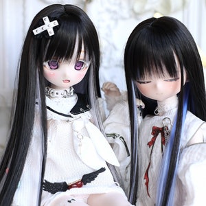 May include: Two dolls with long black hair with white and blue streaks. The dolls are wearing white sweaters and have different accessories. One doll has a white cross hair clip and the other has a red bow.