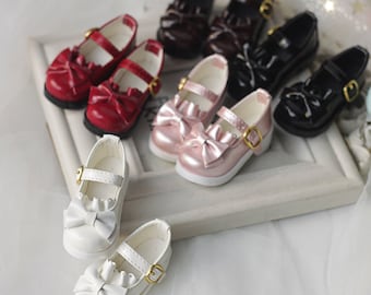 Può includere: Un set di otto scarpe in miniatura per bambole con fiocchi e fibbie. Le scarpe sono di vari colori, tra cui bianco, rosa, rosso e nero.