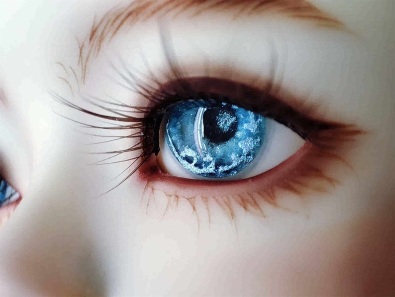 May include: Close-up of a blue eye with a white and blue iris. The eye is surrounded by long eyelashes and a brown eyebrow.