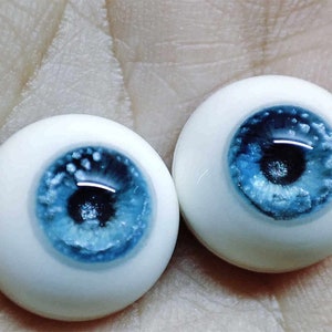 May include: Two blue and white glass doll eyes with a white iris and a blue pupil. The eyes have a speckled, glittery effect.
