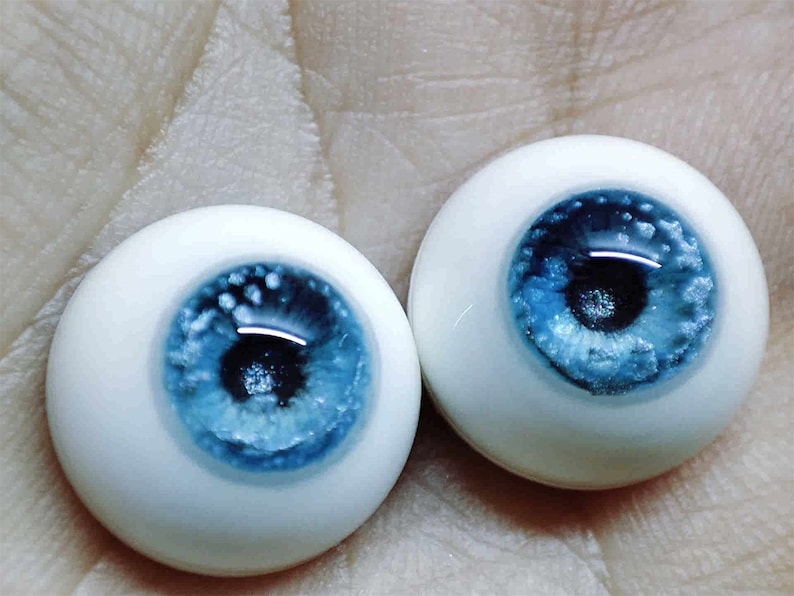 May include: Two blue and white glass doll eyes with a white iris and a blue pupil. The eyes have a speckled, glittery effect.