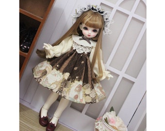 May include: A brown and cream doll dress with a white lace collar and a brown and white patterned skirt. The doll is wearing a white lace hat with a brown ribbon.