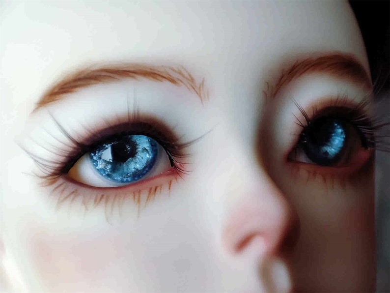May include: Close-up of a doll's face with blue eyes and brown eyelashes. The doll's eyes have a swirling, galaxy-like pattern.