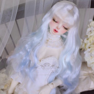 May include: A doll with long, wavy, white and light blue hair. The doll is wearing a white dress with lace trim.