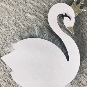 K&ouml;nnte beinhalten: Eine wei&szlig;e schwanf&ouml;rmige Dekoration mit einer goldenen Glitzerkrone und schwarzen Augendetails. Der Schwan hat einen flauschigen wei&szlig;en Federakzent und ist an einem Holzstab befestigt. Dieser Dekorationsartikel ist wahrscheinlich f&uuml;r eine Party oder Veranstaltung.
