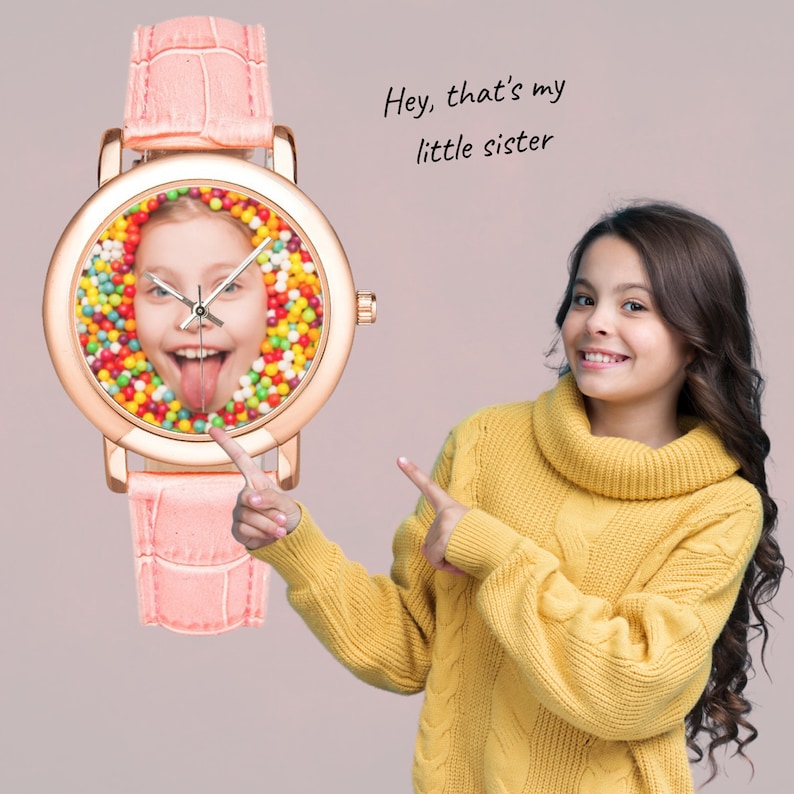 May include: A pink wristwatch with a round face featuring a colorful candy-like design and a picture of a girl's face in the center. The text "Hey, that's my little sister" is written above the watch.