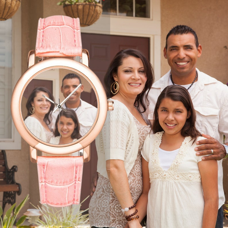 May include: A pink wristwatch with a rose gold face. The face of the watch has a picture of a family of three. The watch has a crocodile-embossed band.