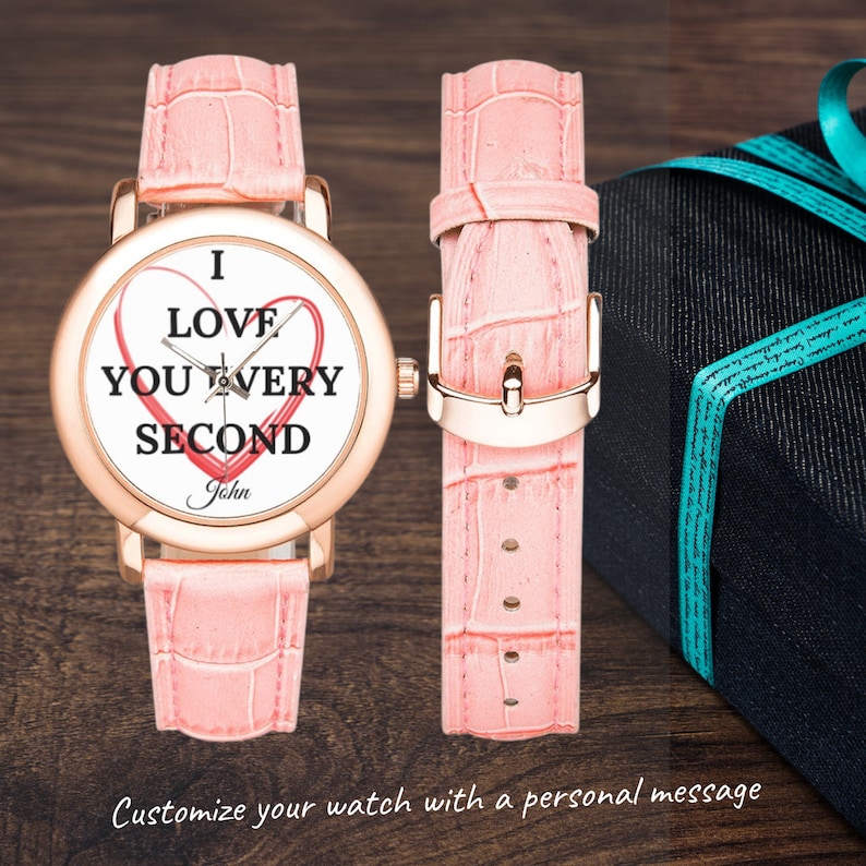 May include: A pink leather wristwatch with a white face and a heart design. The watch face says "I love you every second" and "John".