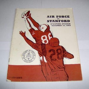 以下が含まれることがあります： エアフォースとスタンフォードのアメリカンフットボールの試合のヴィンテージプログラム。プログラムには、2人の選手がアクションを起こしている赤と白のイラストが描かれています。プログラムのテキストには、「Air Force vs Stanford, Stanford Stadium, November 15, 1969」と記載されています。
