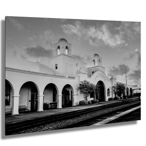 May include: A black and white photograph of a historic train station with a white facade and arched doorways. The station is called "Orlando" and is located in front of a set of railway tracks.