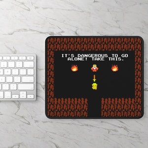 May include: A black and red mousepad with a pixelated image of a video game character. The text on the mousepad reads "It's dangerous to go alone! Take this."