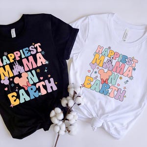 May include: Two t-shirts with the text "Happiest Mama on Earth" in rainbow colors. The shirts feature a cartoon image of Mickey Mouse's head with a castle in the background.