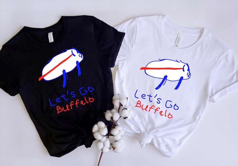 May include: Two t-shirts, one black and one white, each featuring a cartoon buffalo design with the text "Let's Go Buffalo." The buffalo is white with a red stripe and blue legs. The text is in blue and red.