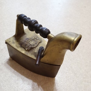 Puede incluir: Plancha antigua de hierro y latón con mango de madera. La plancha tiene un diseño decorativo con el texto "Dresdner Werkstätten" y un escudo.