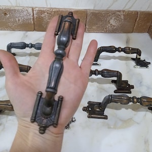 Peut inclure: Une collection de poignées de porte de style antique avec des détails ornés. Les poignées sont en métal et ont une finition bronze foncé.