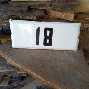 Metallic white enamel plate with the number 18.The enamel plate is attached to the wall of the house or to the fence.of the USSR-1970s.