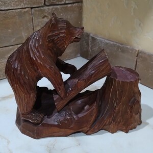 Statue of a wooden bear on a log.Figurine of a forest brown bear made of wood.Handmade souvenir.Sculpture of a wooden carved bear on a stand