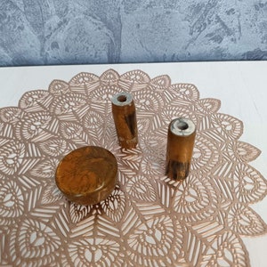 May include: Three resin bottle stoppers in a gold and brown colour scheme. The stoppers are round and have a hole in the top. They are sitting on a gold lace doily.