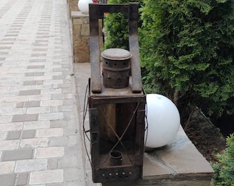 May include: A rusty metal lantern with a white globe on a stone wall. The lantern has a handle and a wire cage around the glass.