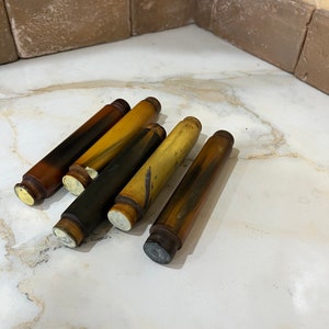 May include: Five wooden dowels with different coloured stains and finishes. The dowels are arranged in a semi-circle on a white surface.