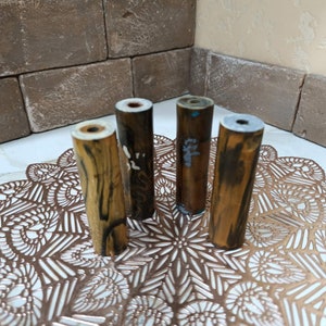 May include: Four wooden dowels with different patterns and colours. The dowels are arranged in a row on a decorative, gold-coloured surface.