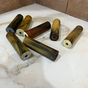 Puede incluir: Una colección de seis clavijas de madera rayadas en marrón, negro y verde. Las clavijas miden aproximadamente 7,5 cm de largo y tienen un acabado liso y pulido.