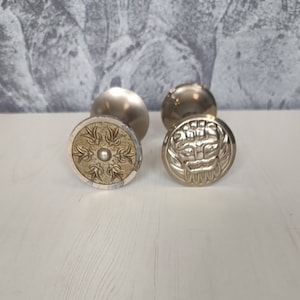 May include: Two silver-toned door knobs with decorative gold accents. One knob features a floral design, while the other has a stylized face.