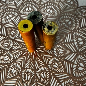 Puede incluir: Tres objetos cilíndricos con centros huecos, dispuestos verticalmente. Uno es de color amarillo brillante sólido, mientras que los otros dos presentan un patrón jaspeado de negro y amarillo. Las superficies son lisas y tubulares, con una abertura.