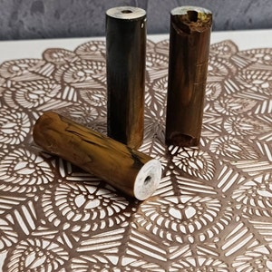 May include: Three wooden dowels with different patterns and colours. The dowels are brown, black, and a mix of brown and gold. They are all approximately 12.5 cm long and have a hole drilled through the centre.